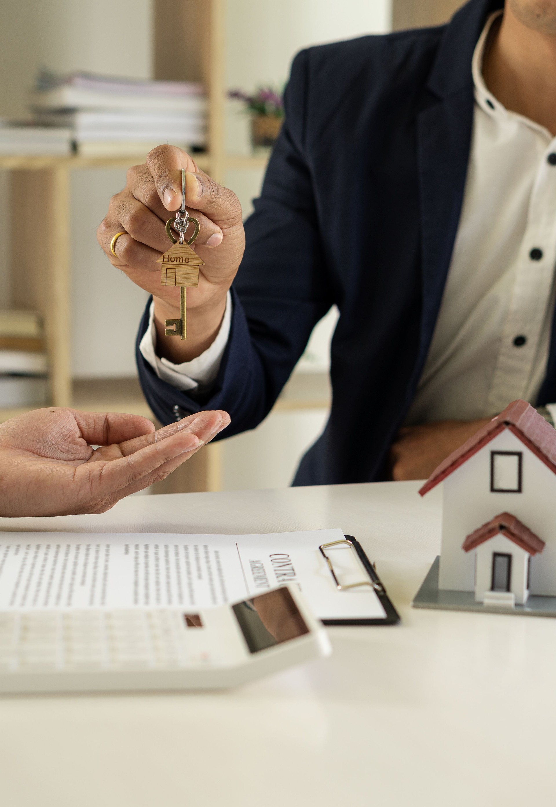 Sales representatives offer home purchase contracts to purchase a house or apartment and give home key chains to customers in the office buying or selling and renting real estate ideas.