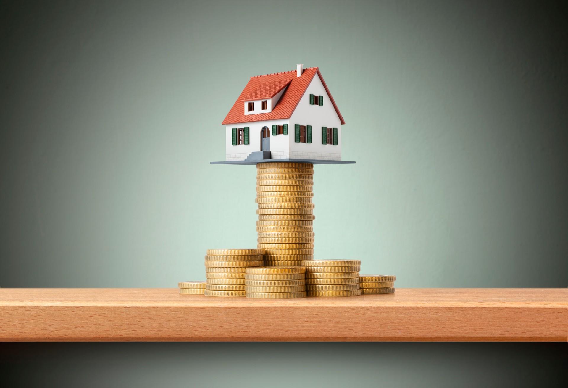 Miniature model house standing on a stack of coins