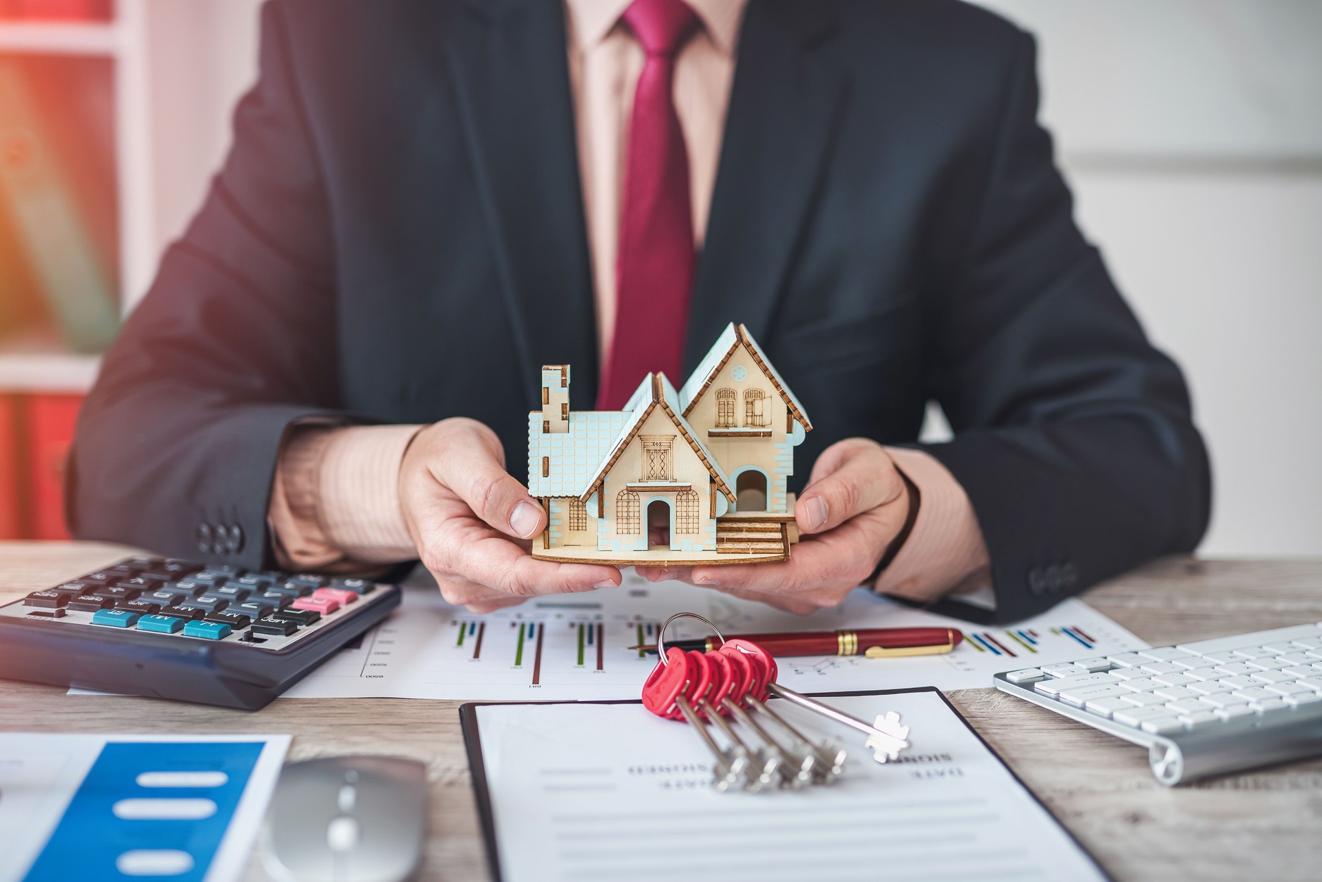 house  man in jacket sitting with documents for house sale contract and keys to house model.